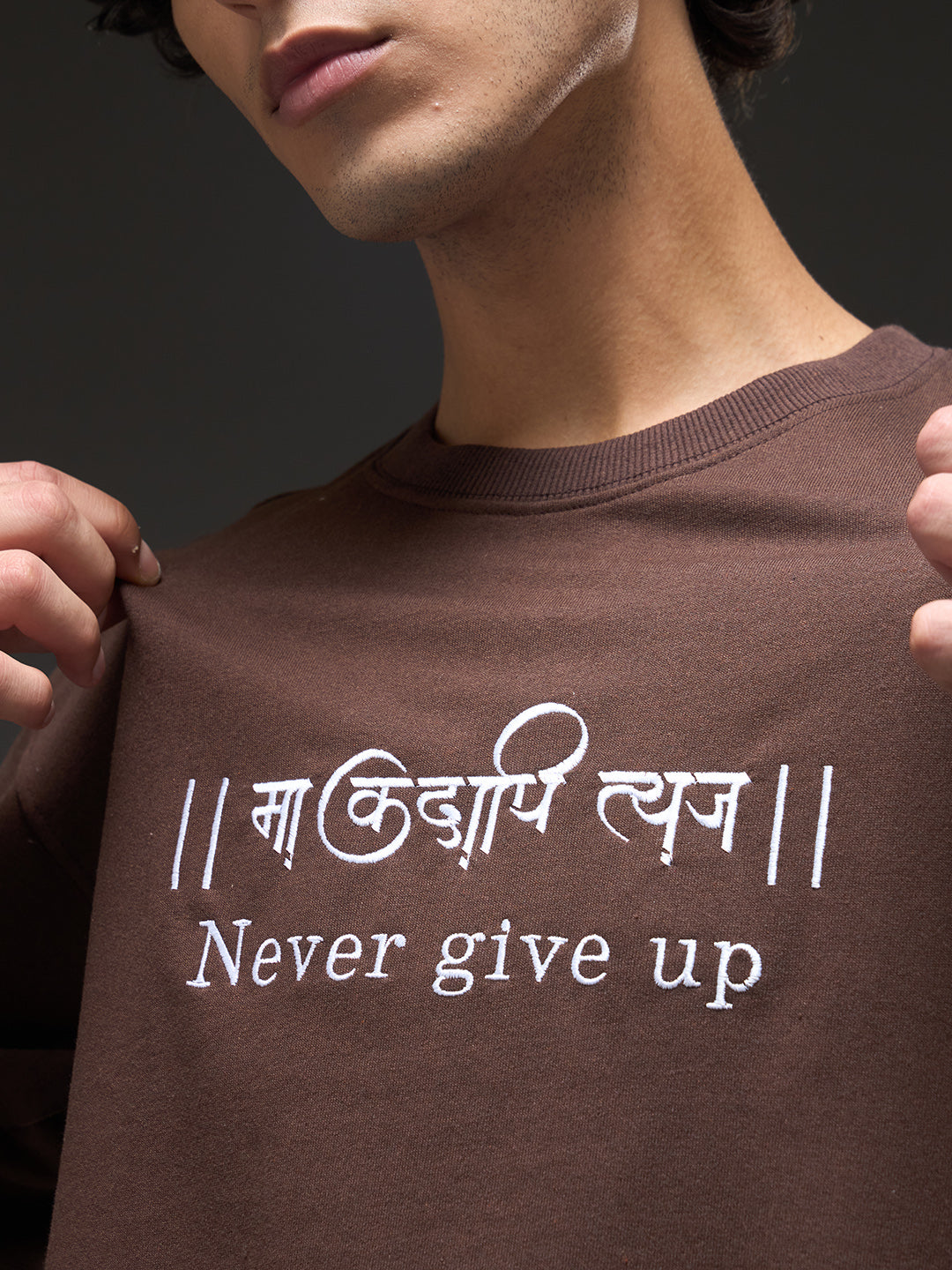 Brown recycled oversized tee by Rudrajap featuring embroidered "Never Give Up" message on soft, eco-friendly fabric.